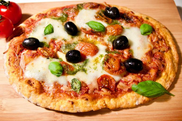 Aceitunas, albahaca y mozzarella cubren una masa de pizza sin gluten con salsa de tomate.